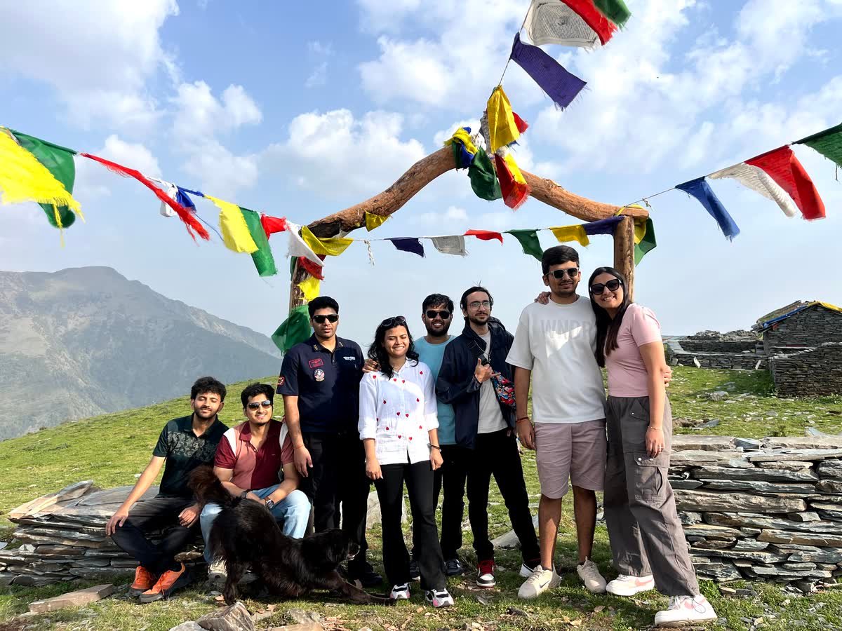 Trekkers gathered under the prayer flag arch at Thatharana with the valley behind