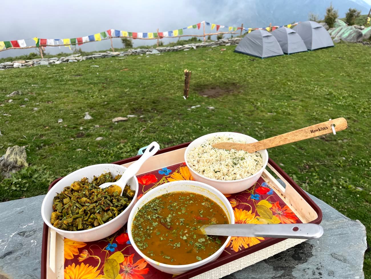 Home-style dal, rice and saag served on a tray with the tents behind