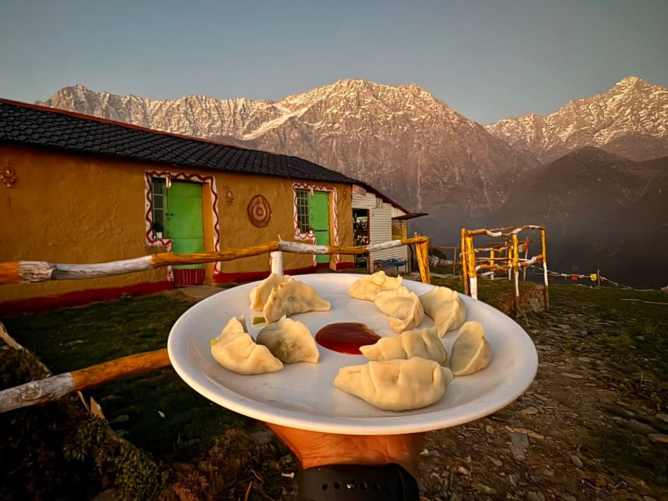 Plate of fresh momos at the campsite as golden hour lights the Dhauladhar peaks