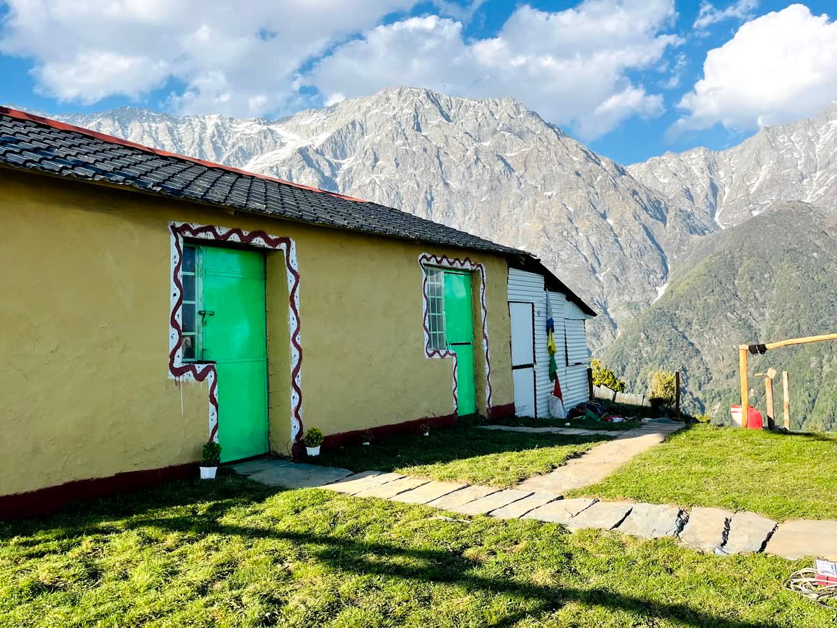Mudhouse rooms with green doors opening onto the lawn and the Dhauladhar range