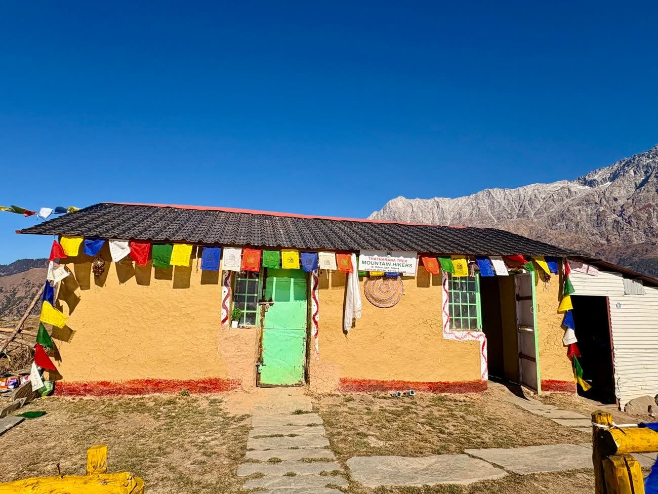 Mudhouse rooms strung with prayer flags below the Dhauladhar range