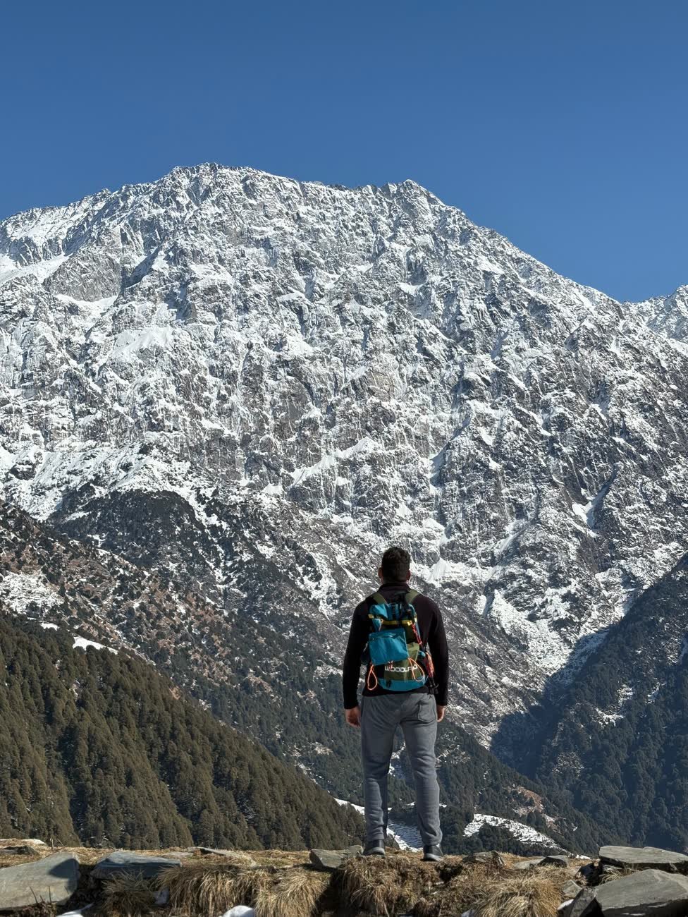 A trekker looking out at the snow-covered Dhauladhar peaks from Thatharana